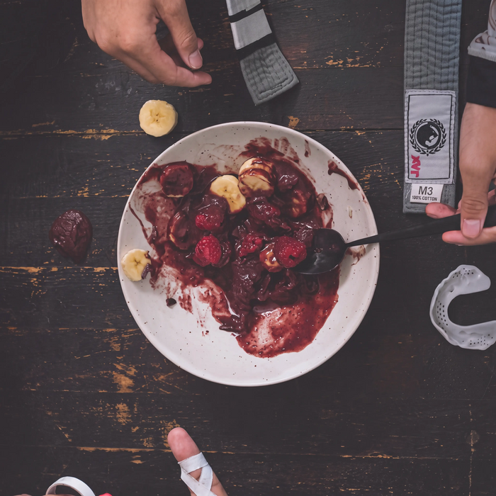 Overhead shot of an açaí bowl with banana and raspberries beside a jiu-jitsu belt and mouthguard