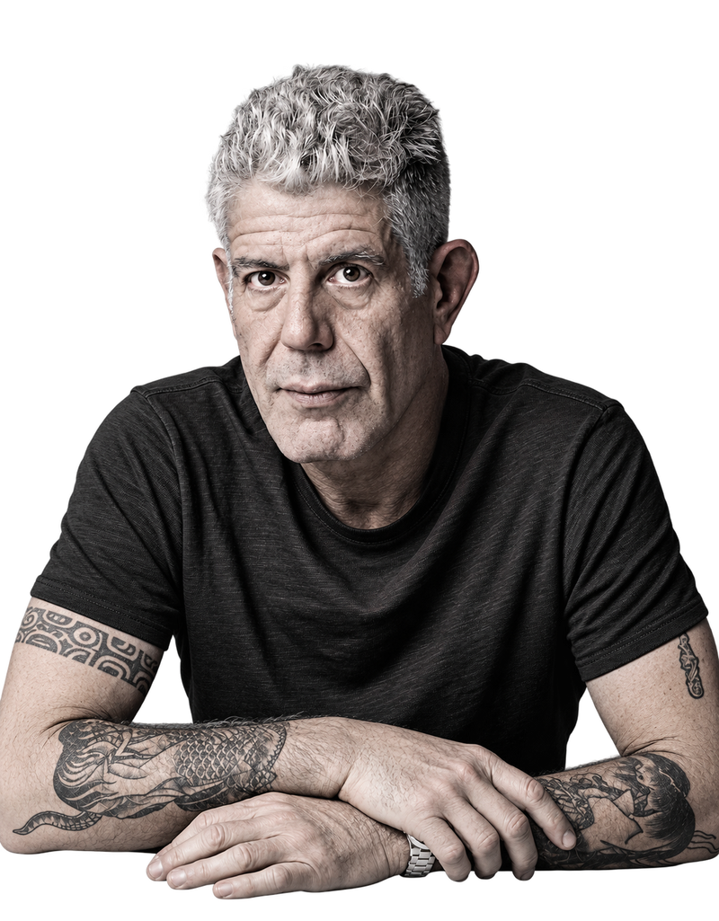 Portrait of Anthony Bourdain in a black t-shirt, arms folded on a table